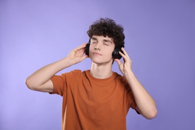Cute teenage boy listening music with headphones on violet background