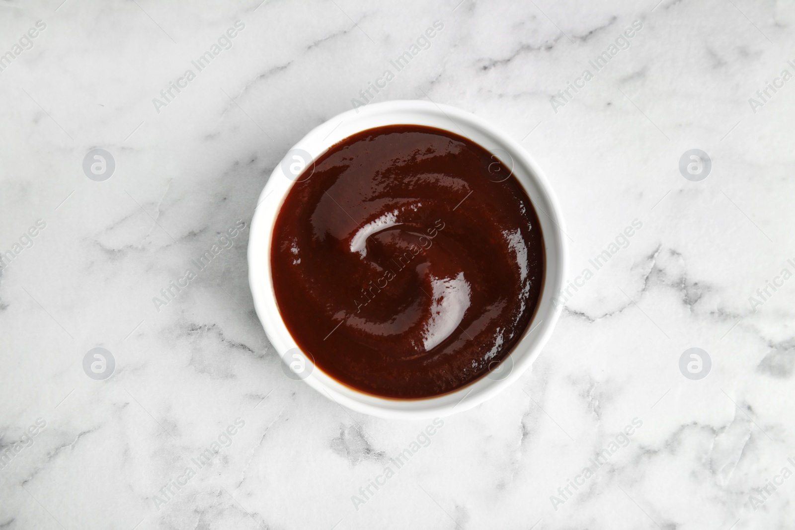 Photo of Barbecue sauce in bowl on marble background, top view