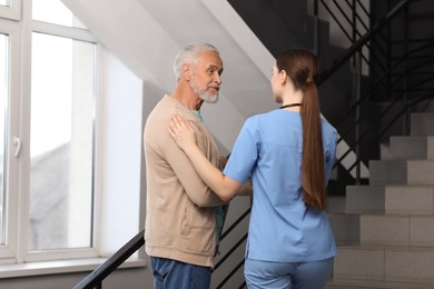 Photo of Young healthcare worker assisting senior man on stairs indoors