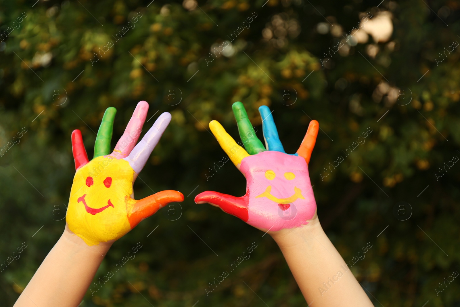 Photo of Kid with smiling face drawn on palms in green park, closeup