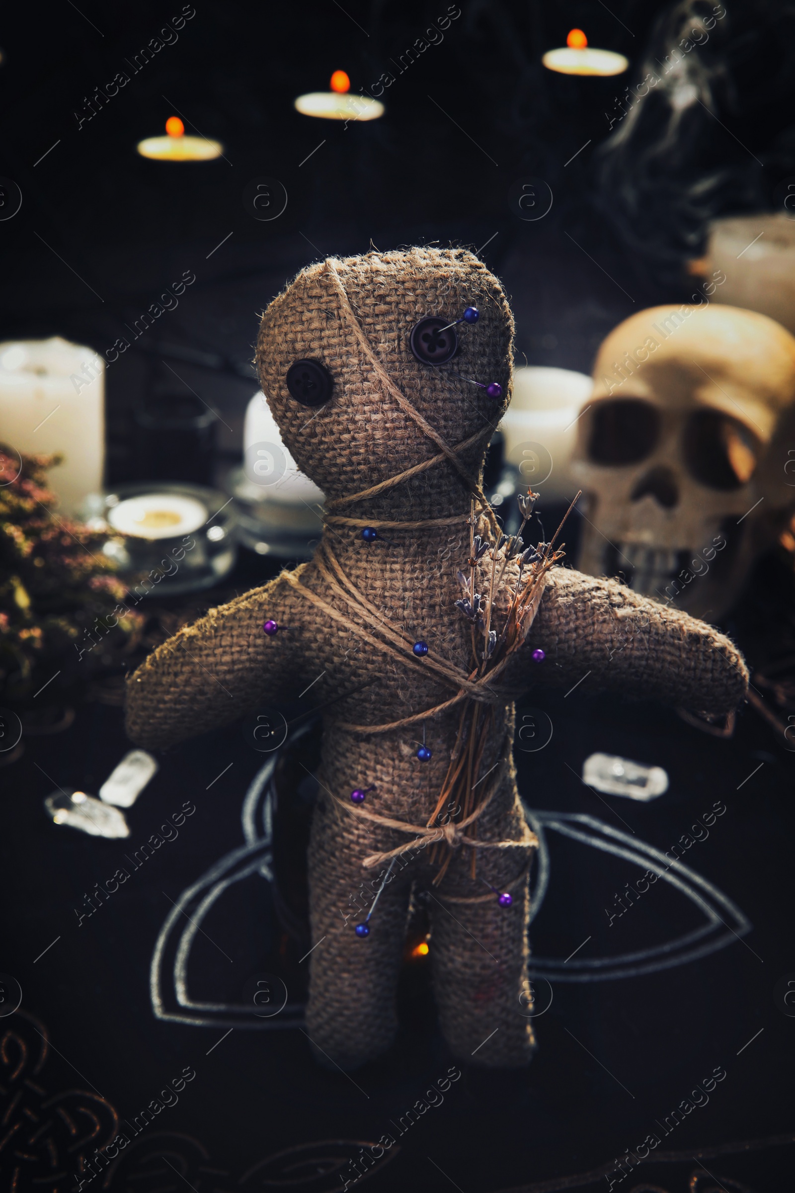 Image of Voodoo doll with pins and dried flowers on table indoors