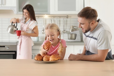 Photo of Happy couple treating their daughter with freshly oven baked bun in kitchen