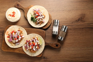 Photo of Delicious tacos with vegetables, meat and sauce on wooden table, flat lay. Space for text