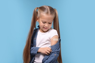 Photo of Girl with sticking plaster on arm after vaccination against light blue background