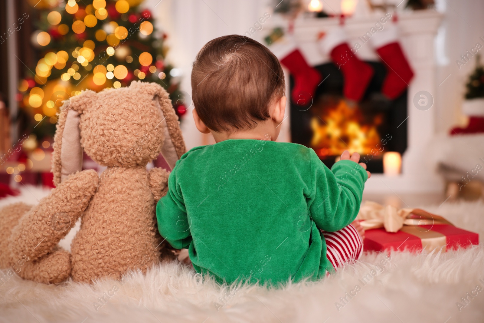 Photo of Baby in elf costume with toy bunny at home, back view. Christmas time