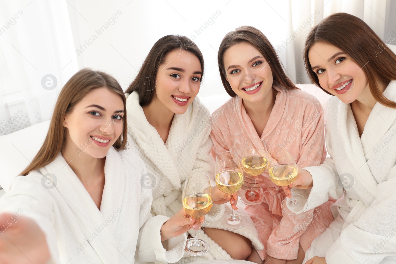 Photo of Beautiful young ladies with glasses of wine taking selfie at pamper party indoors. Woman's Day