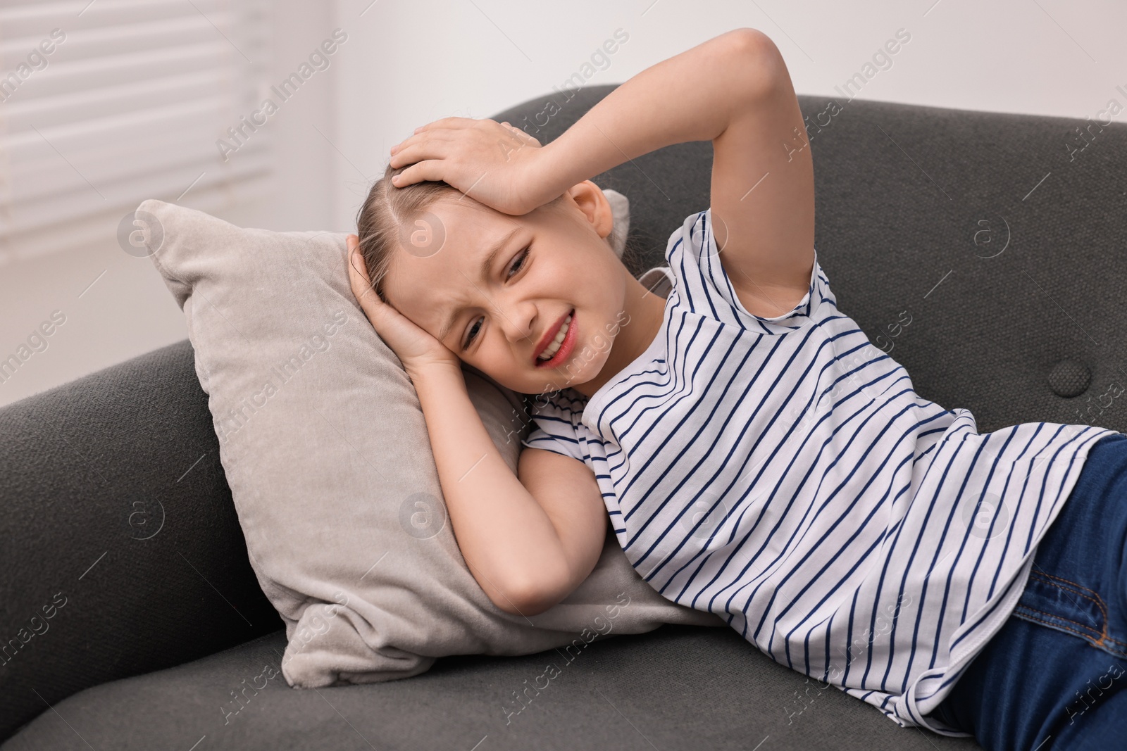 Photo of Little girl suffering from headache on sofa indoors