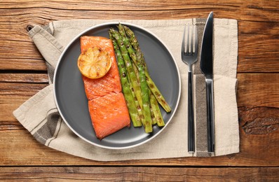 Photo of Tasty grilled salmon with asparagus and lemon served on wooden table, top view