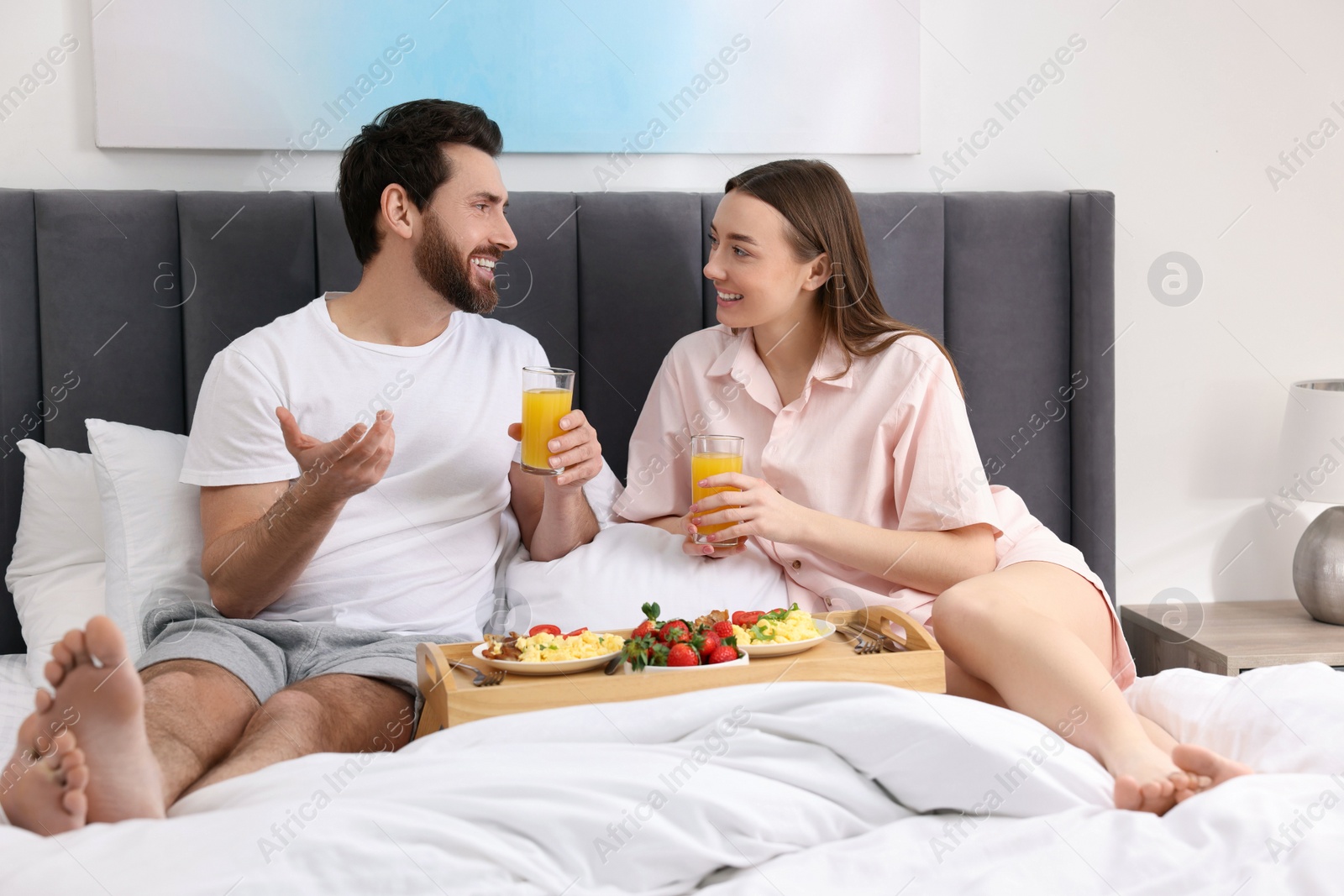 Photo of Happy couple having breakfast and talking on bed at home