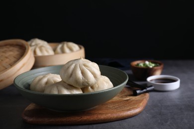 Photo of Delicious bao buns (baozi) in bowl on grey textured table, closeup