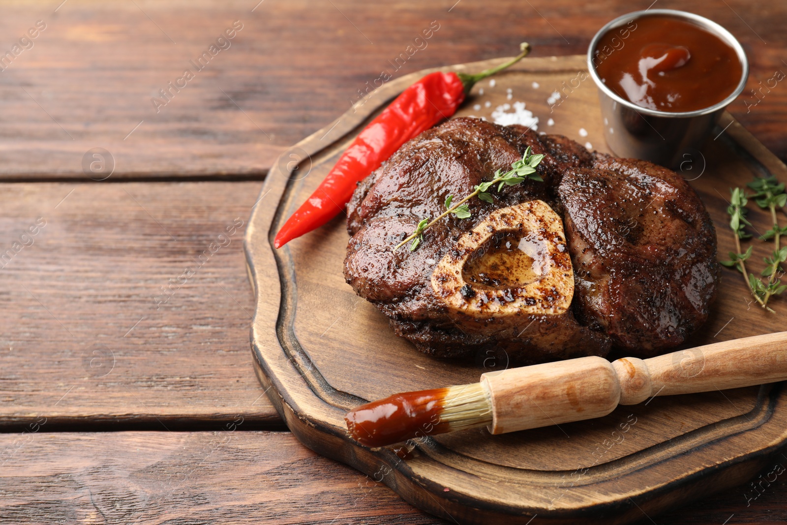 Photo of Delicious roasted beef meat served with sauce and spices on wooden table. Space for text