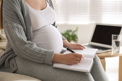 Photo of Pregnant woman working on sofa at home, closeup. Maternity leave