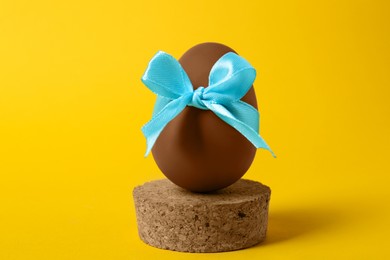 Photo of Tasty chocolate egg with light blue bow on orange background