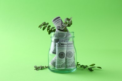 Photo of Financial savings. Dollar banknotes in glass jar and twigs on green background