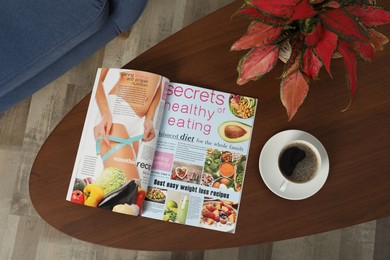 Photo of Open magazine, cup of coffee and houseplant on wooden table indoors, top view
