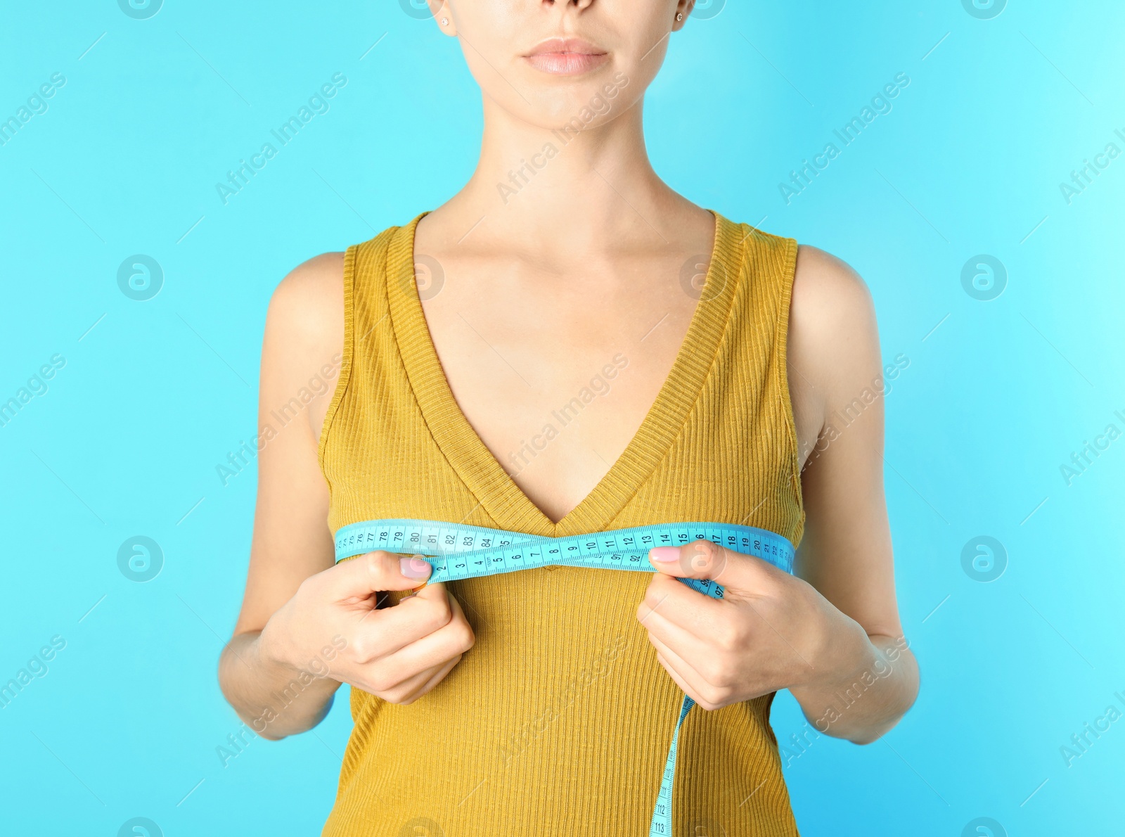 Photo of Young woman measuring breast size on color background, closeup. Cosmetic surgery