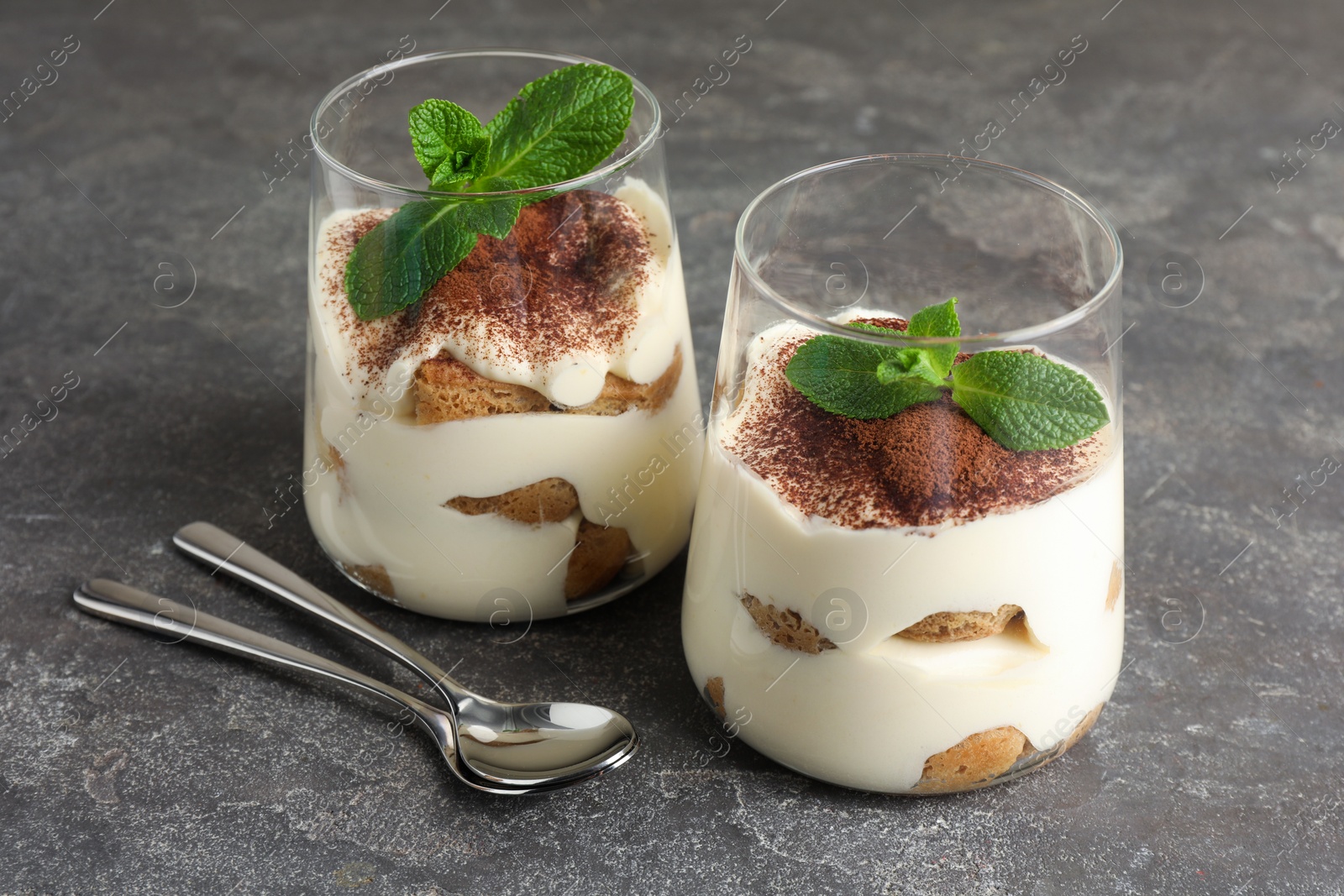 Photo of Delicious tiramisu with mint in glasses on grey table