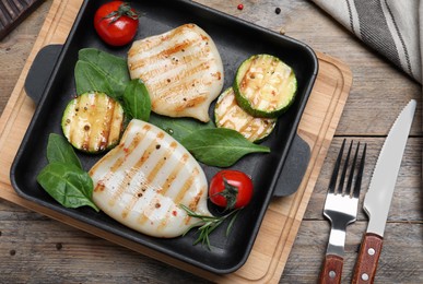 Photo of Grilled squid tubes with vegetables served on wooden table, flat lay
