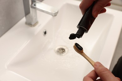 Photo of Man applying charcoal toothpaste onto toothbrush in bathroom, closeup