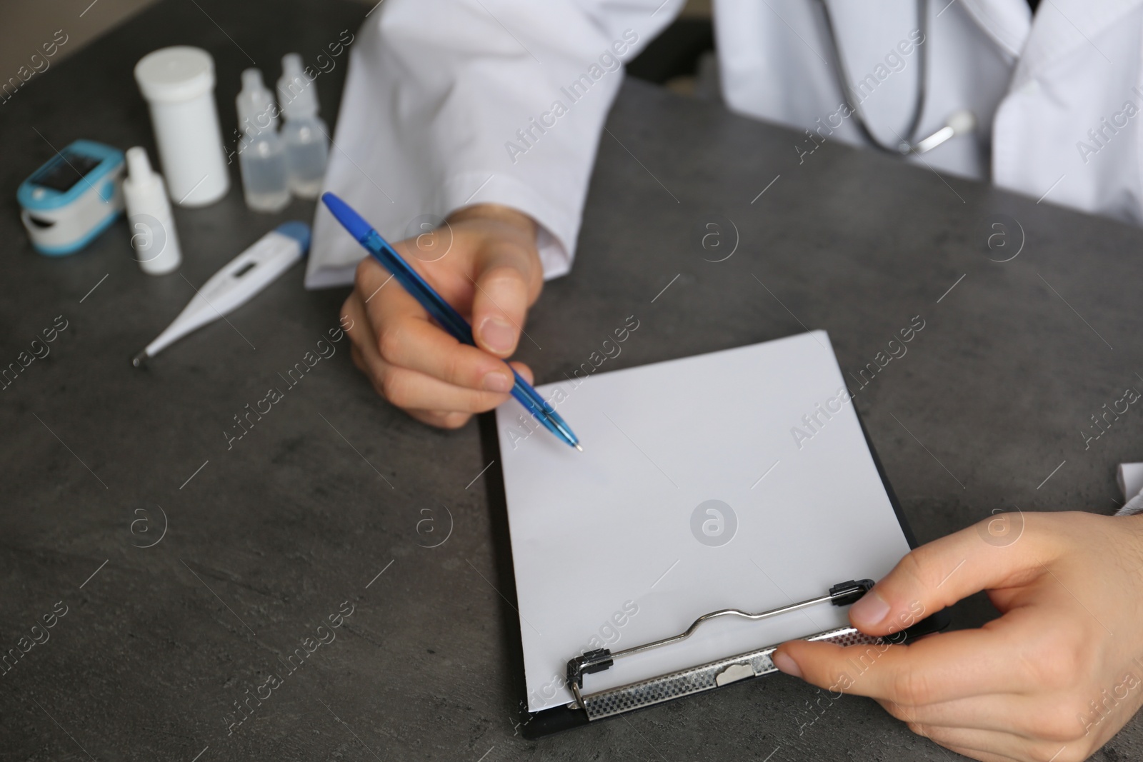 Photo of Doctor writing at table with different medical objects, closeup with space for text