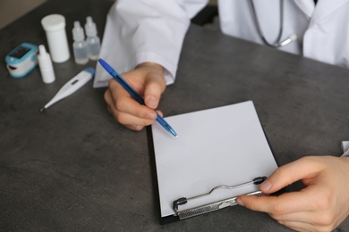 Photo of Doctor writing at table with different medical objects, closeup with space for text