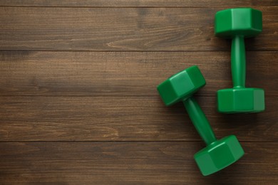 Green dumbbells on wooden table, flat lay. Space for text