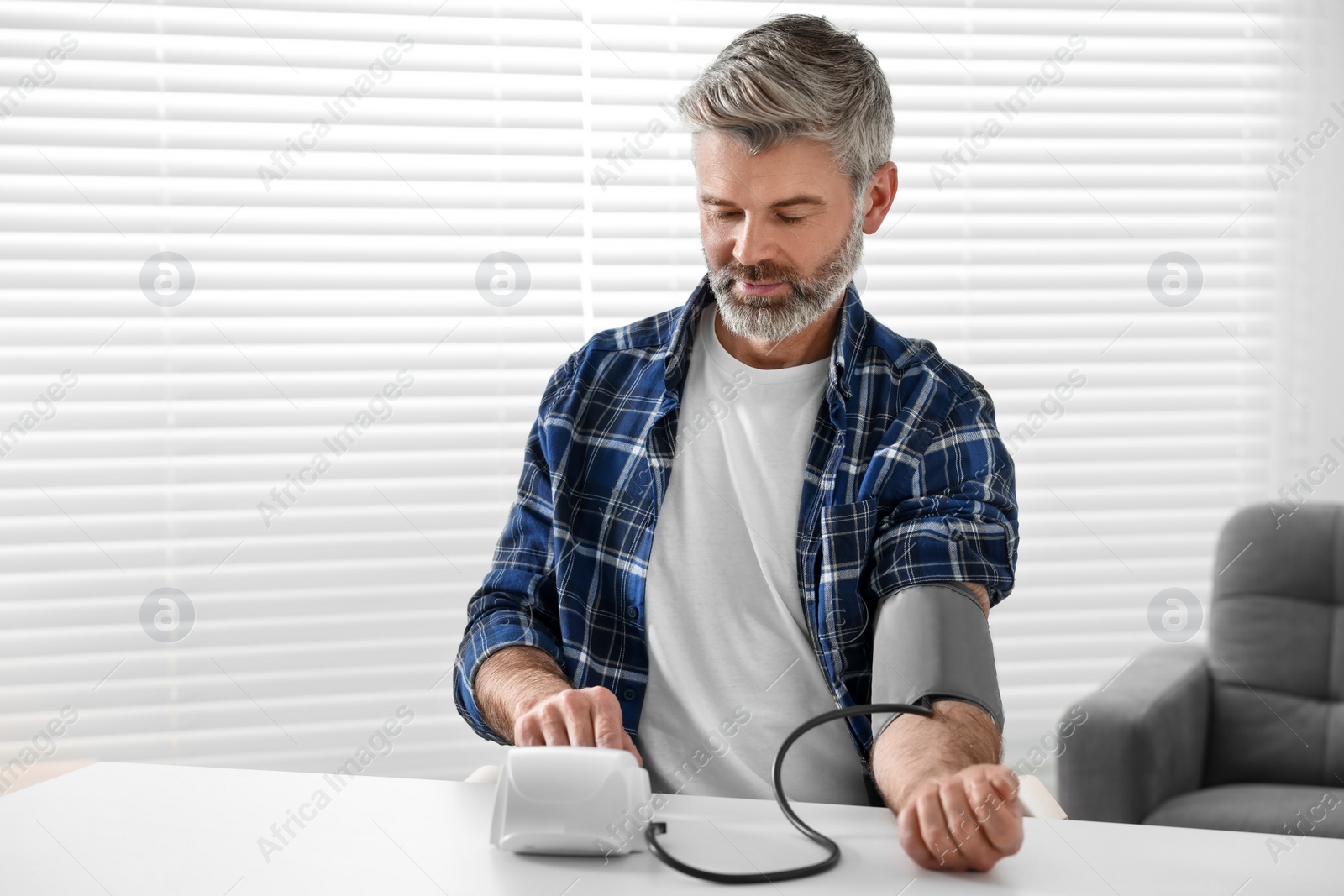 Photo of Man measuring blood pressure at table indoors