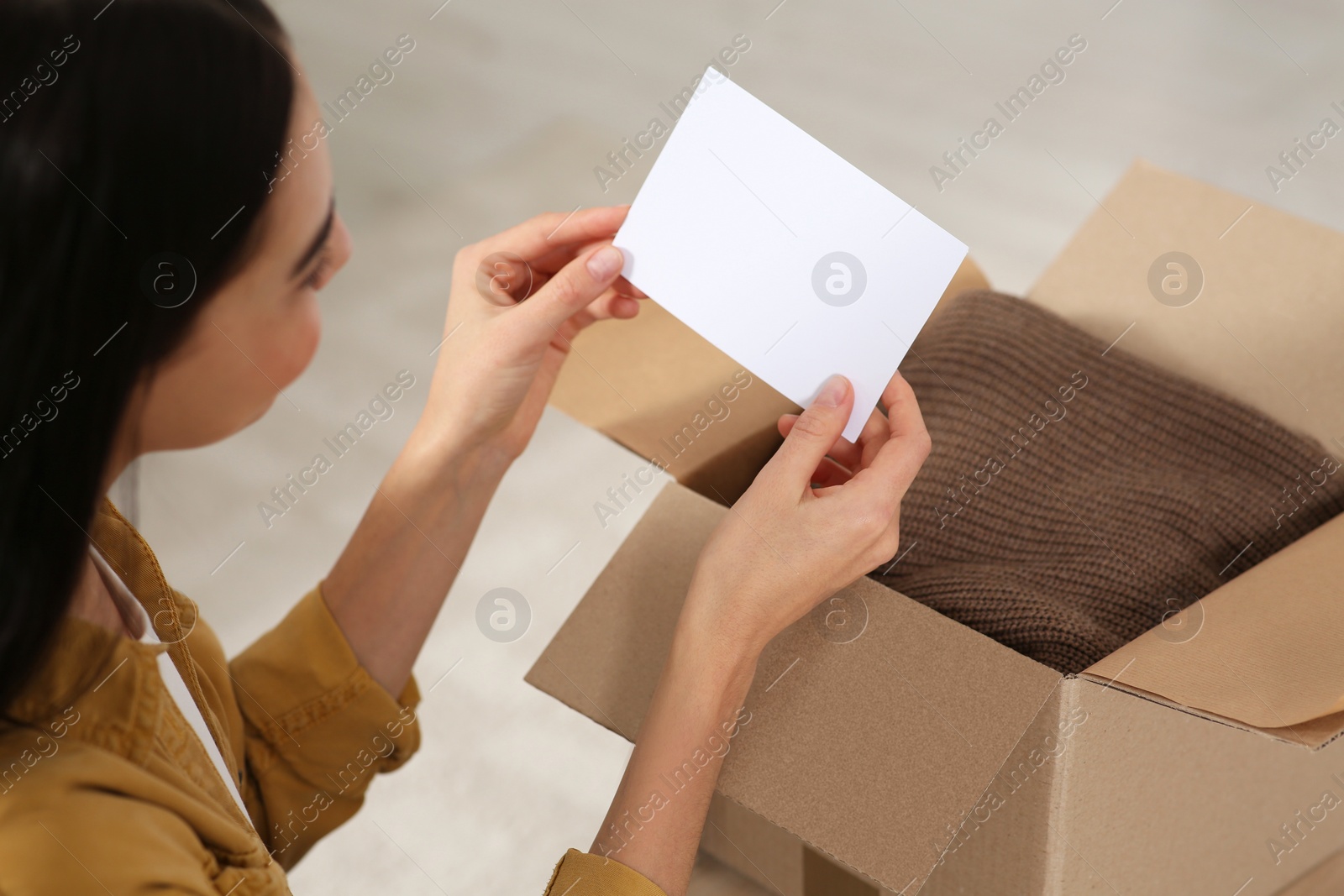 Photo of Woman holding greeting card near parcel with Christmas gift indoors, closeup