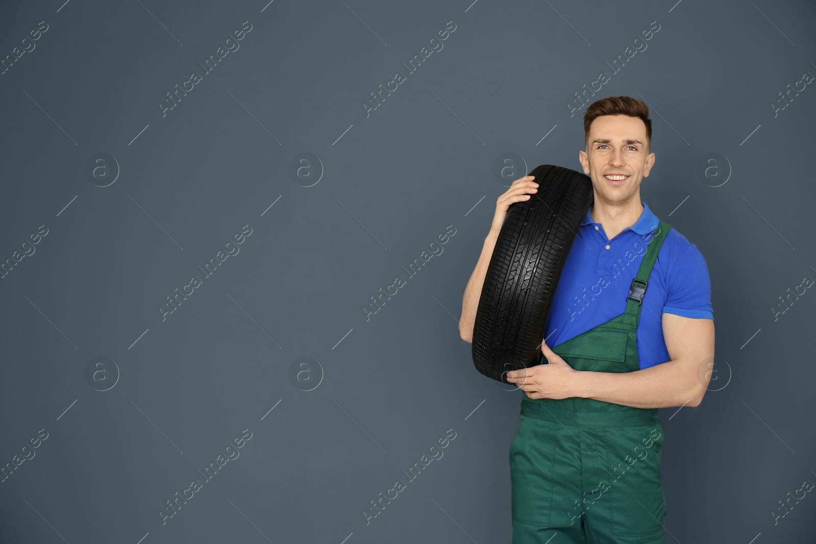 Photo of Male mechanic with car tire on grey background