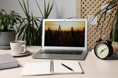 Photo of Modern laptop, office supplies, cup of coffee and alarm clock on white table indoors