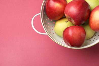 Colander with fresh apples on pink table, top view. Space for text