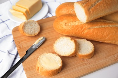 Photo of Tasty cut baguette with fresh butter on white table