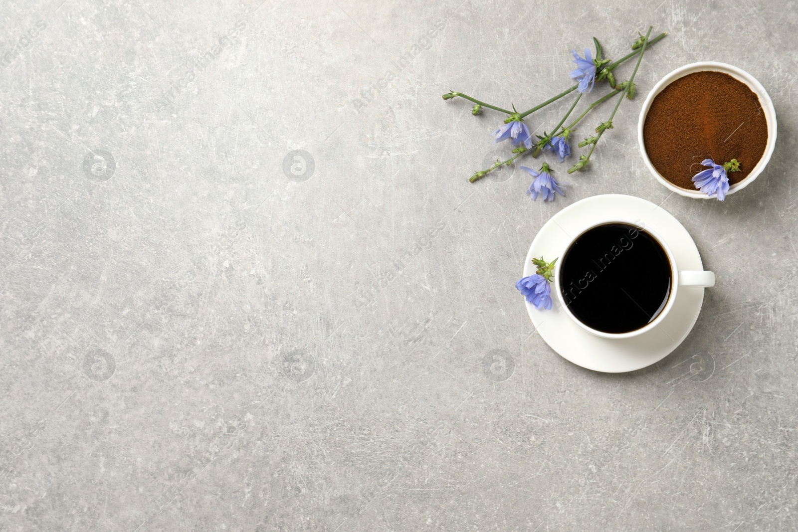 Photo of Cup of delicious chicory drink, powder and flowers on light grey table, flat lay. Space for text