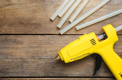 Photo of Yellow glue gun and sticks on wooden table, flat lay. Space for text