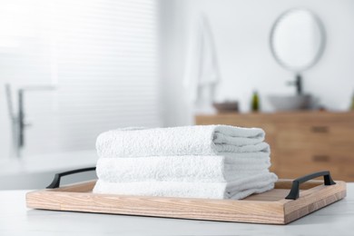 Photo of Wooden tray with stacked bath towels on white table indoors