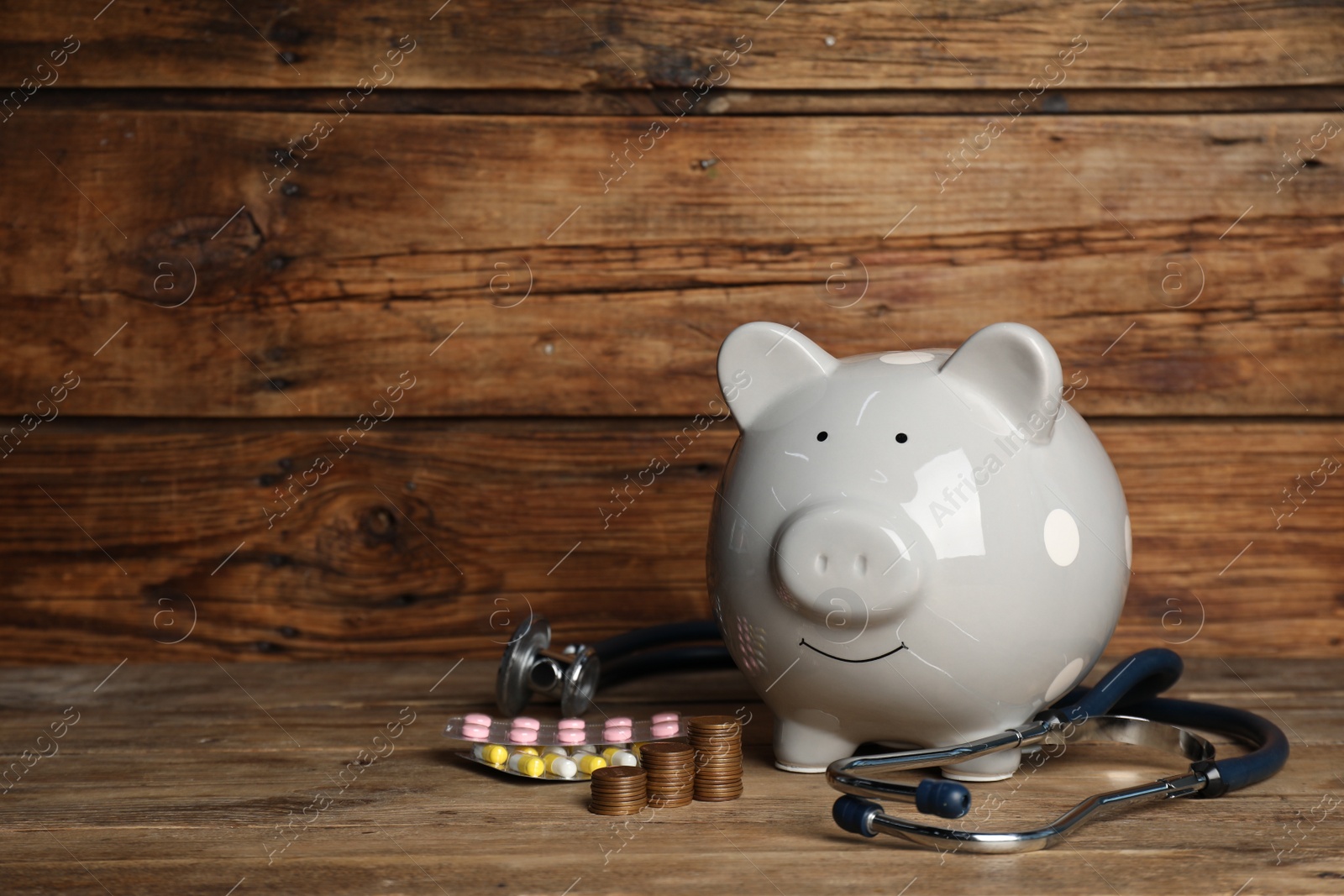 Photo of Light gray ceramic piggy bank, stacked coins and stethoscope on wooden table, space for text. Medical insurance