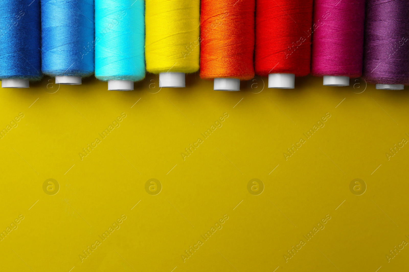 Photo of Set of different colorful sewing threads on yellow background, flat lay. Space for text