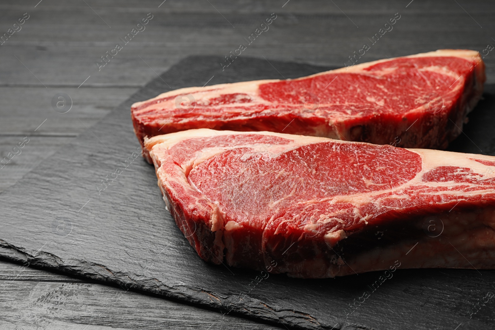 Photo of Slate plate with fresh beef meat on black wooden table, closeup