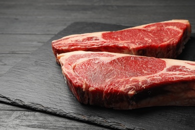 Slate plate with fresh beef meat on black wooden table, closeup