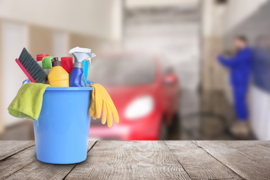 Bucket with cleaning supplies on wooden surface at car wash. Space for text