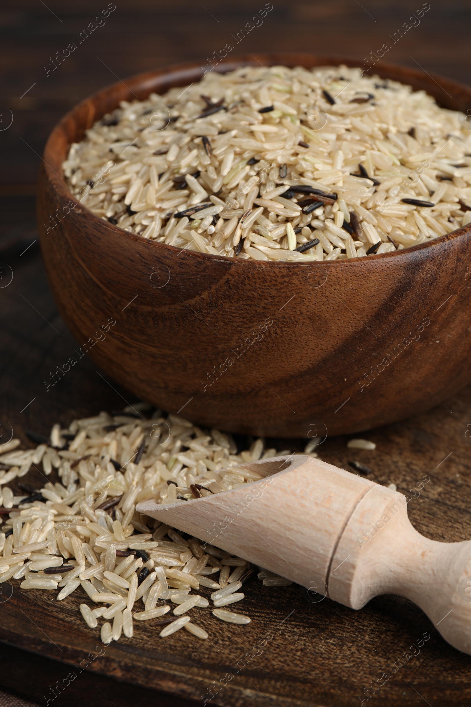 Photo of Wooden dishware with raw unpolished rice on table, closeup