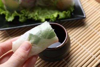 Woman dipping delicious spring roll into soy sauce at table, closeup