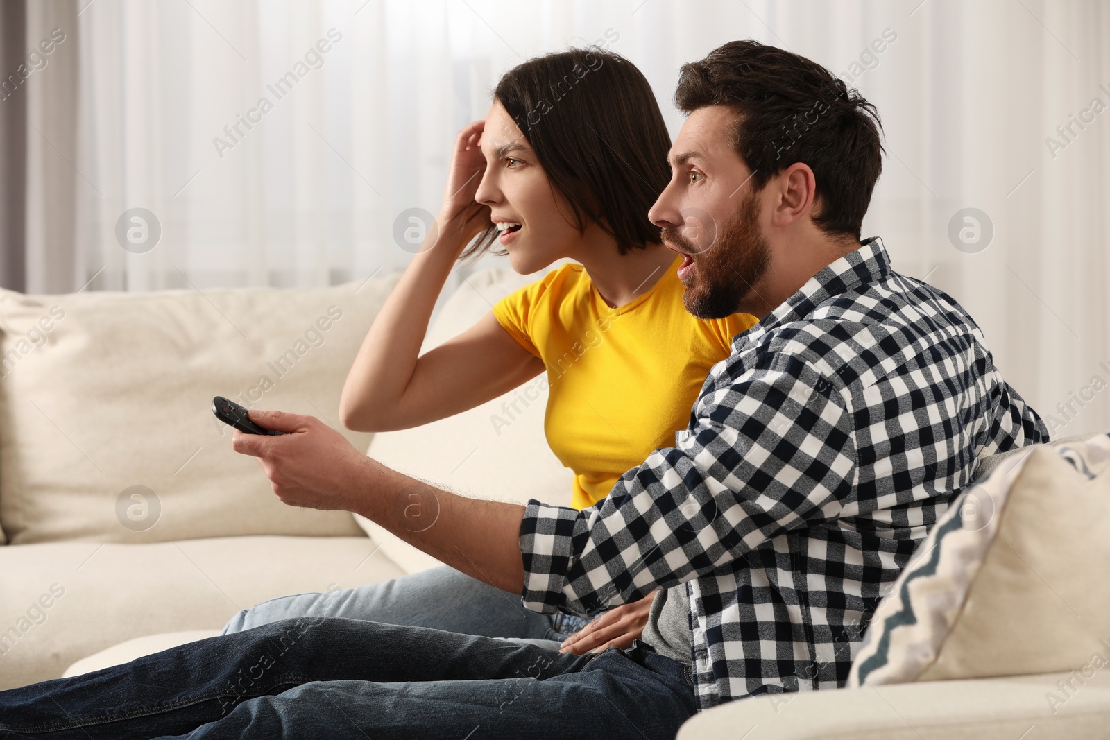 Photo of Surprised couple watching TV on sofa at home