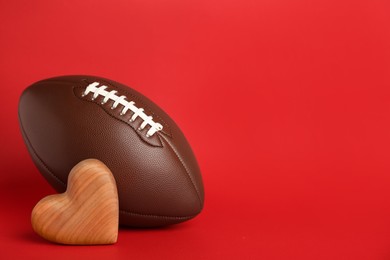 Photo of American football ball and heart on red background. Space for text