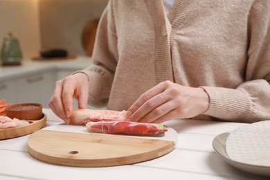 Woman making delicious spring roll at white wooden table, closeup