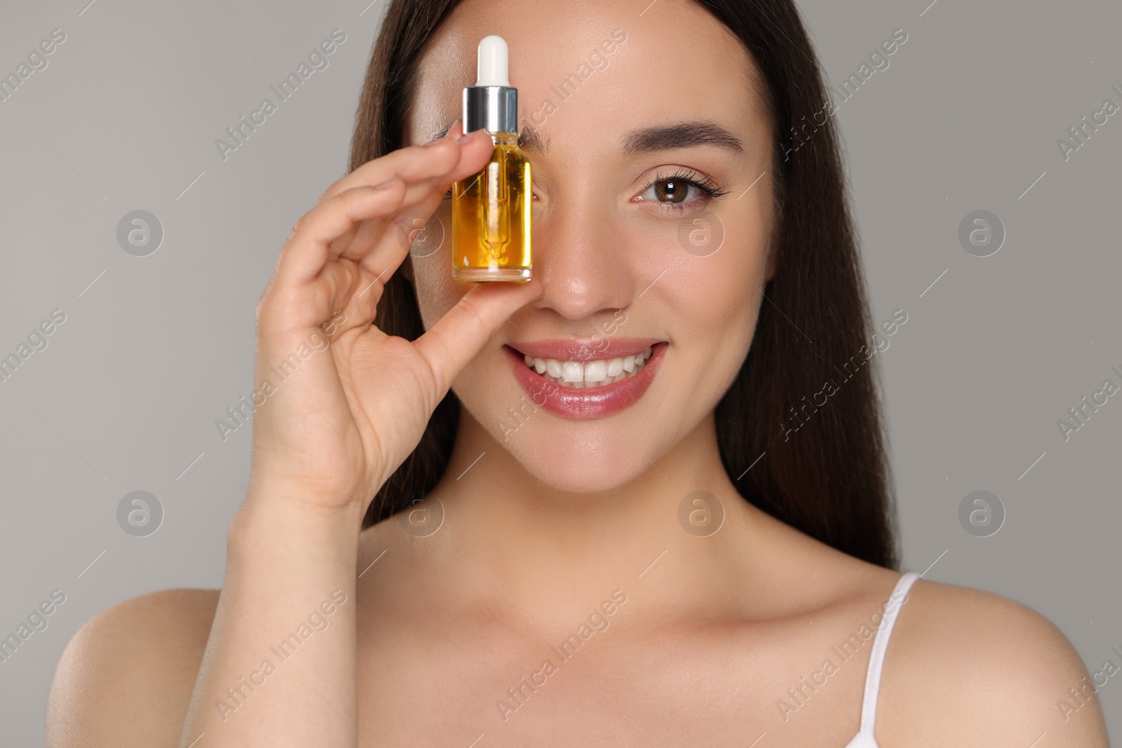 Photo of Beautiful young woman with essential oil on light grey background, closeup