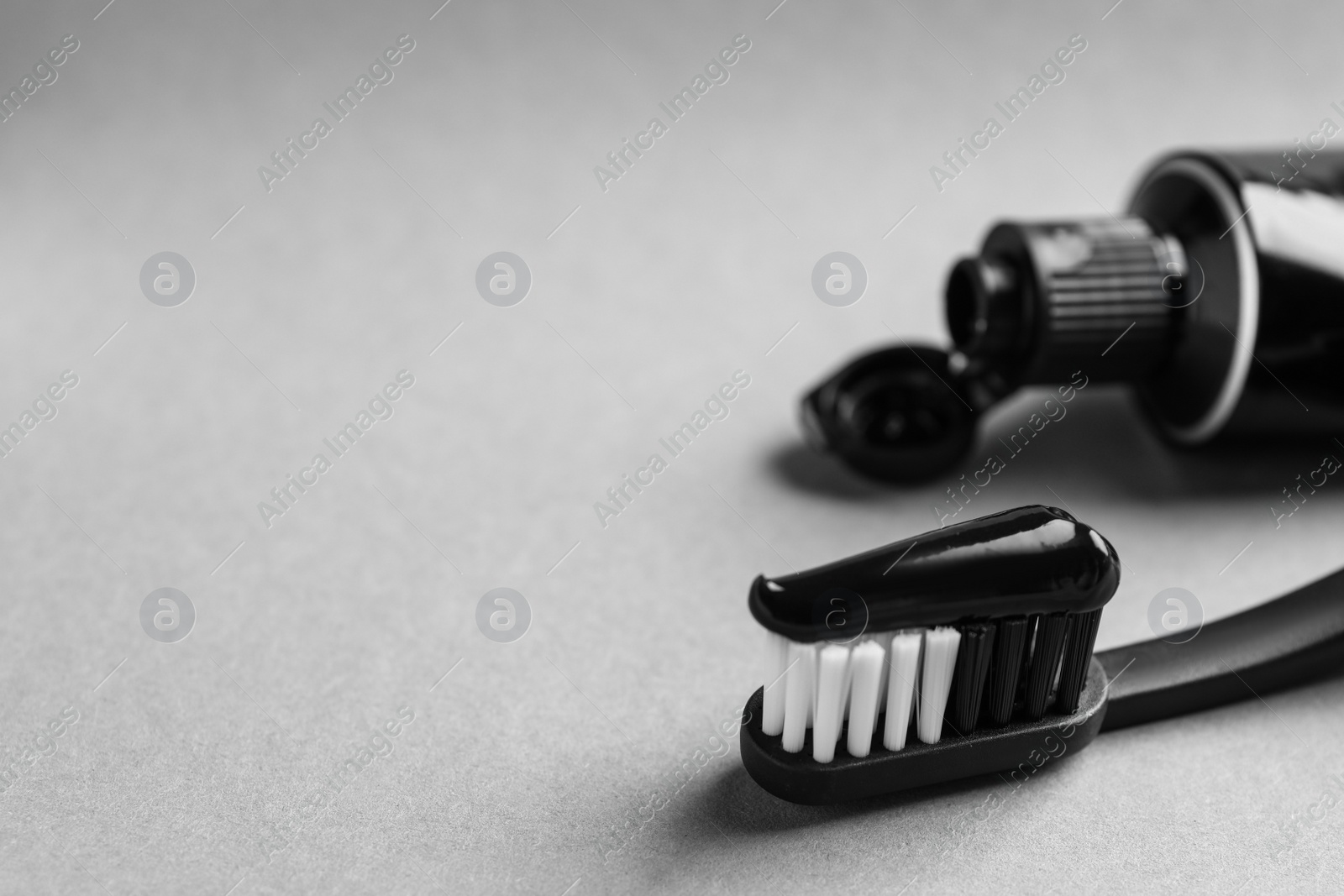 Photo of Brush with charcoal toothpaste on light grey background, closeup. Space for text