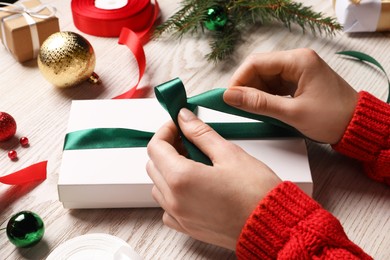 Photo of Woman decorating gift box at white wooden table, closeup. Christmas present