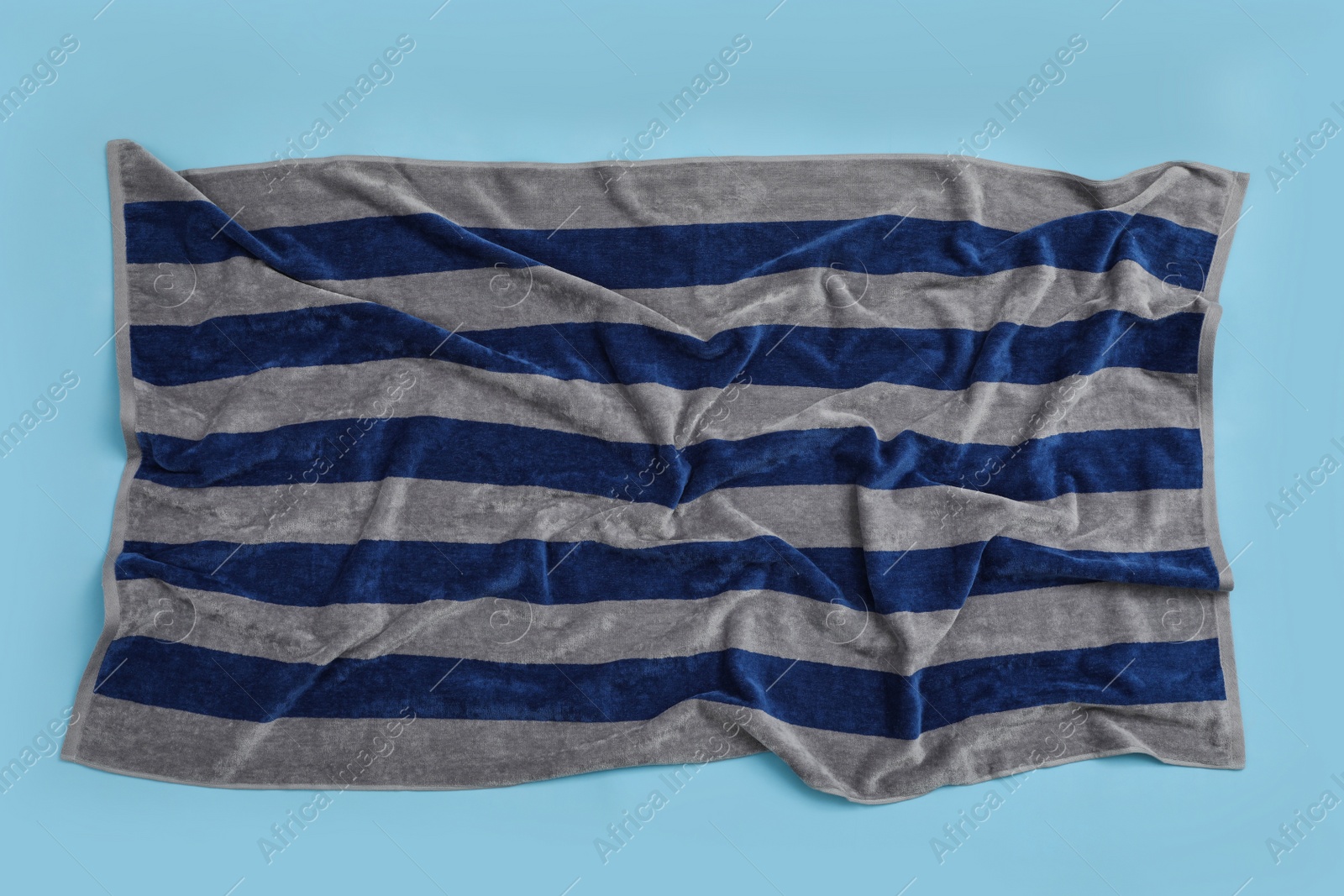 Photo of Crumpled striped beach towel on light blue background, top view