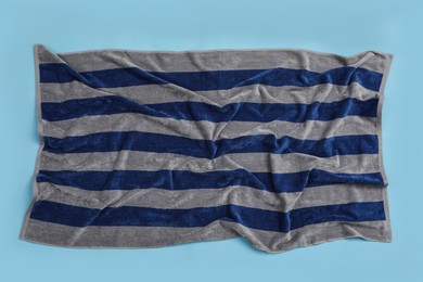 Photo of Crumpled striped beach towel on light blue background, top view